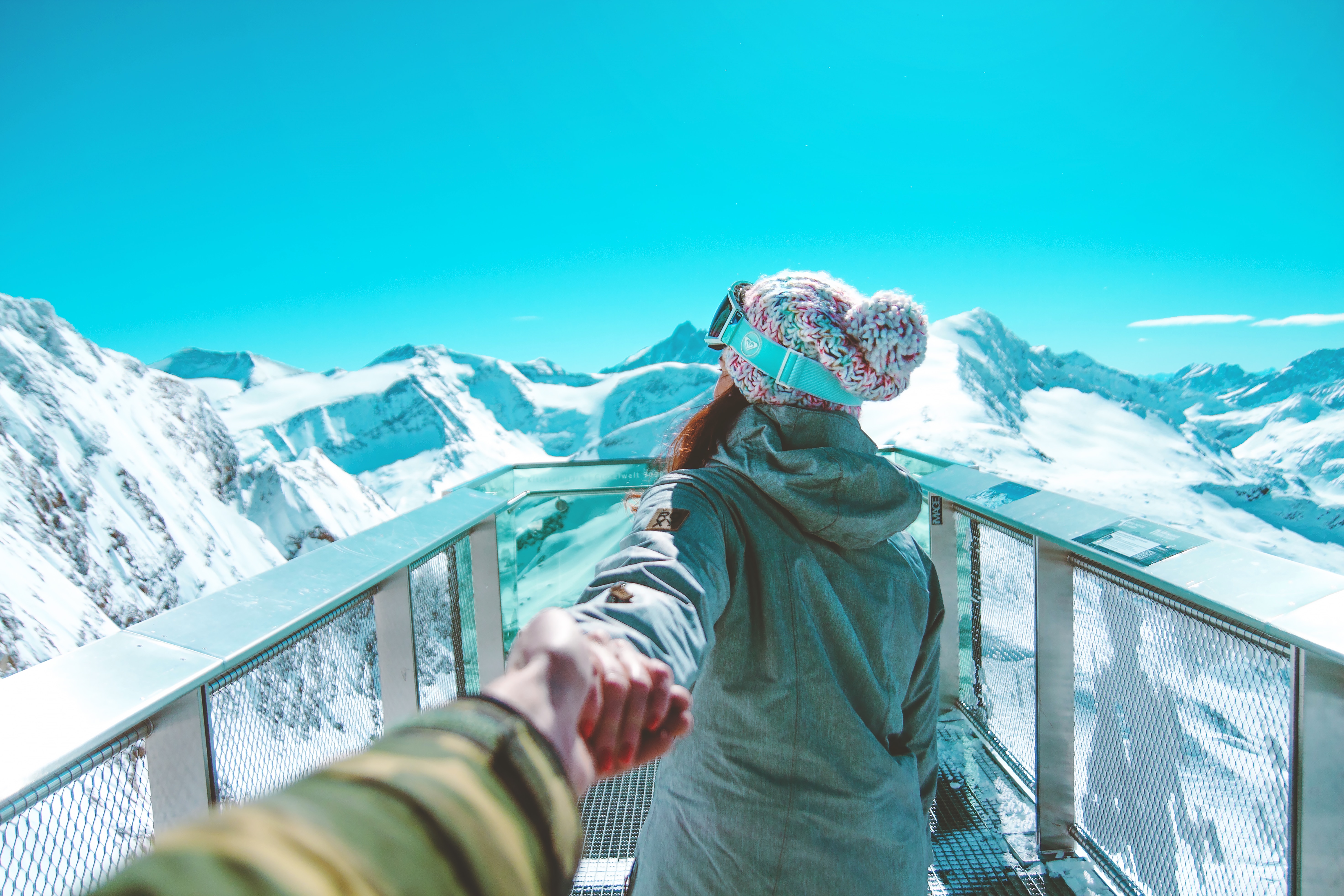 Photo of a couple holding hands admiring the view from a lookout point on top of a snowy mountain